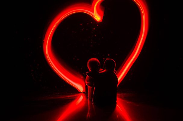 Two young lovers paint a heart on fire. Silhouette of couple and Love words on a dark background - Photo, Image