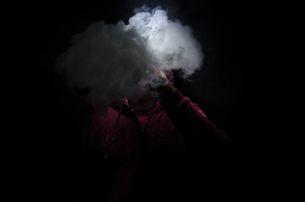 Vaping mężczyzna trzymając mod. Chmurę pary wodnej. Czarne tło. Vaping elektroniczny papieros z dużo dymu. - Zdjęcie, obraz