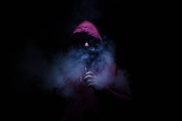 Vaping άνθρωπος που κρατά ένα mod. Ένα σύννεφο των ατμού. Μαύρο φόντο. Ηλεκτρονικό τσιγάρο με πολύ καπνό καπνίσματος. - Φωτογραφία, εικόνα