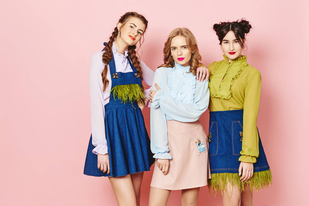 Három fiatal lány pózol, mint rózsaszín háttér stúdióban divatfotózás - Fotó, kép