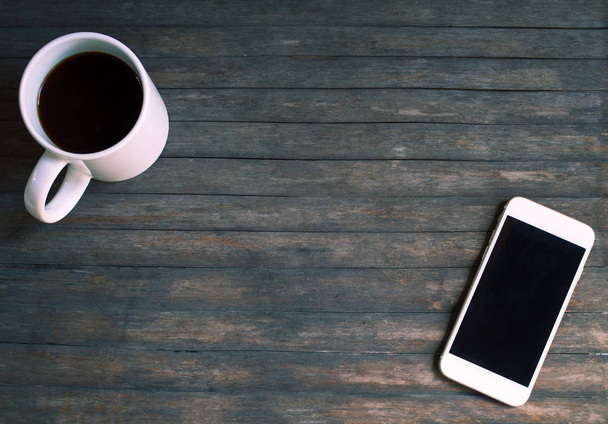 Mug of coffee and a white phone on grey wood background. - Φωτογραφία, εικόνα