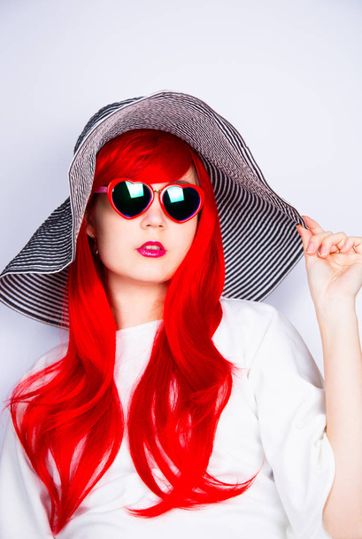 Привлекательная рыжая молодая женщина в солнечных очках и шляпе на белом
 - Фото, изображение