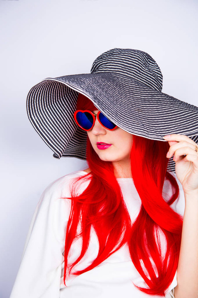 Attractive red-haired young woman in sunglasses and hat on white - Zdjęcie, obraz