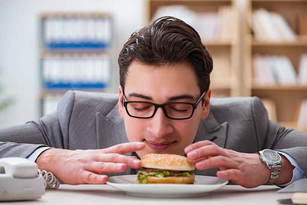 Голодний смішний бізнесмен їсть бутерброд з нездоровою їжею
 - Фото, зображення