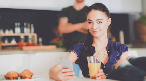 Happy couple using smartphone sitting in kitchen - Photo, image