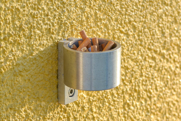 Wandmontierte Zigarettenschachtel aus Edelstahl an einer Außenwand außerhalb eines Arbeitsplatzes, an dem das Rauchen drinnen verboten ist. Dies ermöglicht es Rauchern, Zigaretten zu löschen und zu entsorgen. - Foto, Bild