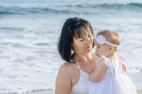 Mother is holding her baby girl on the sandy beach  - Photo, Image