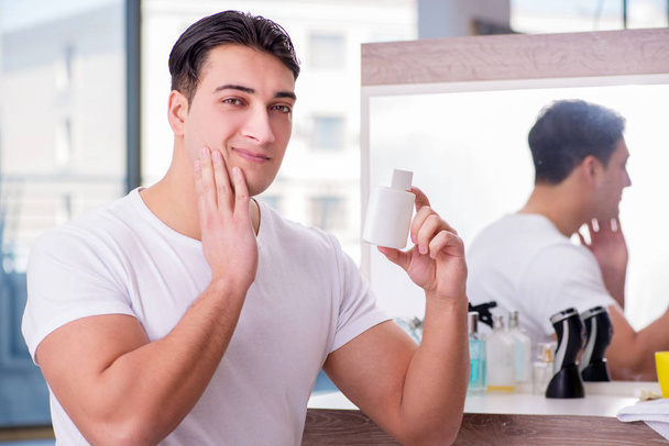Joven hombre guapo aplicando crema facial - Foto, imagen