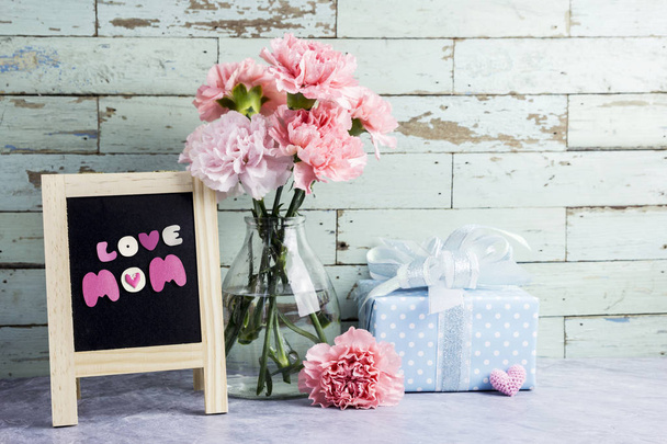 Mothers day concept of pink carnation flowers in clear bottle and gift box and love mom text on blackboard - Photo, Image