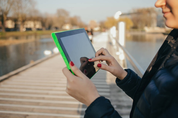 Uśmiechający się młoda kobieta, student, taping na tablecie, za pomocą tabletu w parku miejskim, w pobliżu rzeki. - Zdjęcie, obraz