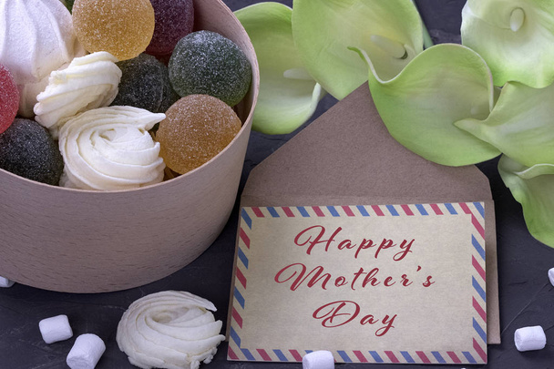 bouquet de callas jaunes verts avec marmelade de guimauves dans une boîte ronde en bois et enveloppe avec lettrage Joyeuse fête des mères sur fond de béton gris
. - Photo, image