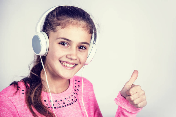 Smiling girl with thumb up listening to music. - Valokuva, kuva