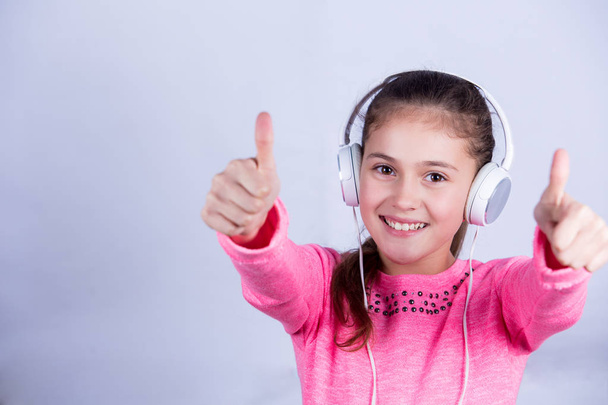 Little girl with thumb up gesture listening to music. - 写真・画像