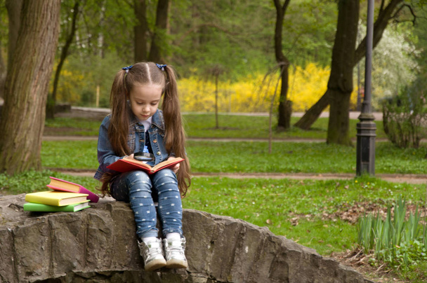 Μικρή μαθήτρια διαβάζοντας ένα βιβλίο στη φύση. Έξυπνο μικρό pupi - Φωτογραφία, εικόνα