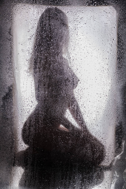 Naked girl behind a wet glass - 写真・画像