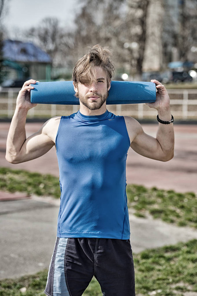 yoga, fitness mat blue color in hands of muscular man - Fotó, kép