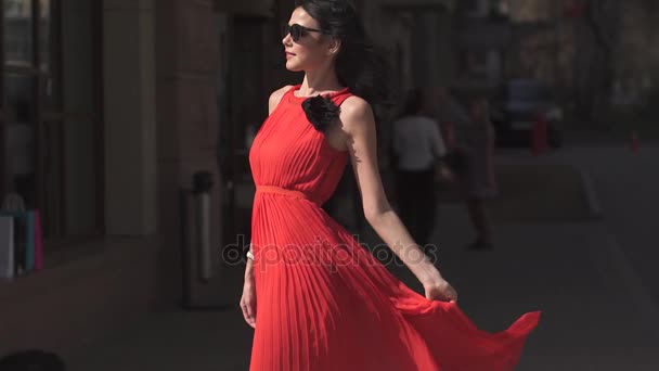 Gyönyörű lány piros ruhában és rajta napszemüveg jelentő, és a városi építészet háttér kamera mosolyogva. - Felvétel, videó
