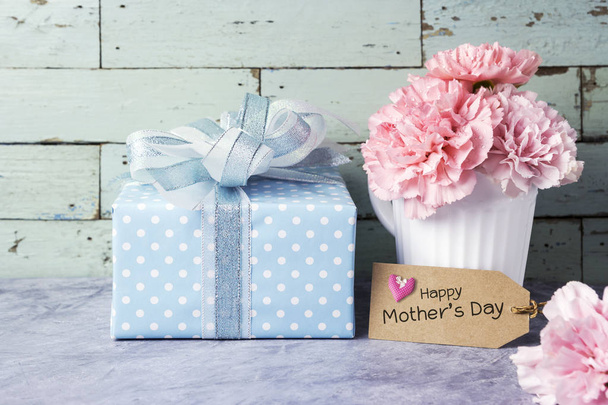 Щасливі матері денне повідомлення на коричневій паперовій мітці та рожева квітка гвоздики в білій чашці та подарунковій коробці
 - Фото, зображення
