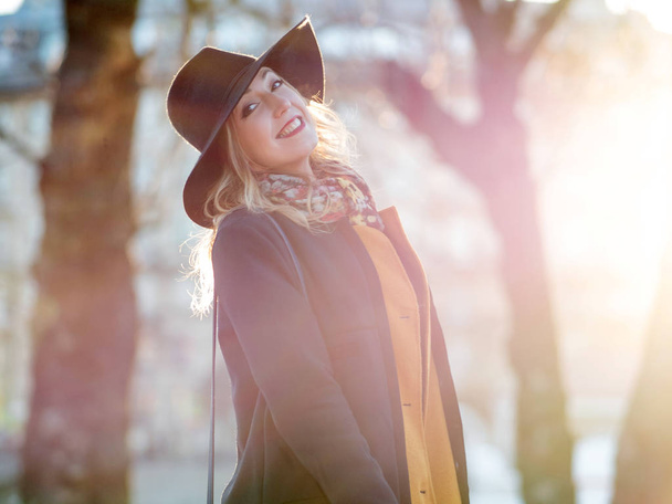 Funny young woman in elegant hat and scarf, walking. Portrait of the charming blonde on the street. Bright sunlight and shading in warm tones - Foto, immagini