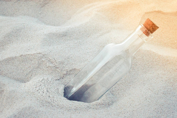 Old vintage empty glass bottle with natural tapered cork lid on the sand beach close-up. - 写真・画像