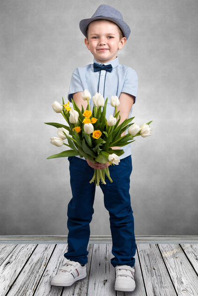 Stylish boy in a hat holding a bouquet of spring tulips.Children's fashion. - Foto, Imagen