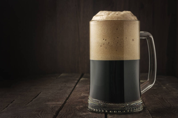 dunkler Bierkrug mit Schaum auf dunklem Hintergrund - Foto, Bild