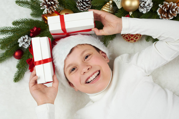 santa kalap öltözött fiú gyermeke kipróbálhassa a szórakoztató karácsonyi dekoráció, arc kifejezése és boldog érzelmek, feküdjön fehér szőr háttér, téli ünnep fogalma - Fotó, kép