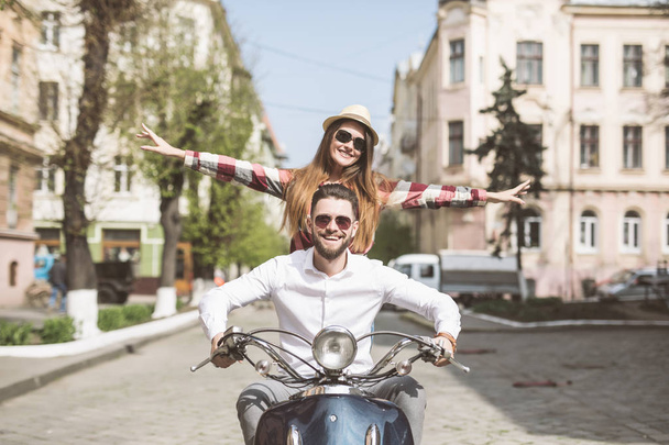 Hermosa pareja joven montando scooter juntos, mientras que la mujer feliz mantener los brazos extendidos y sonriendo
 - Foto, imagen