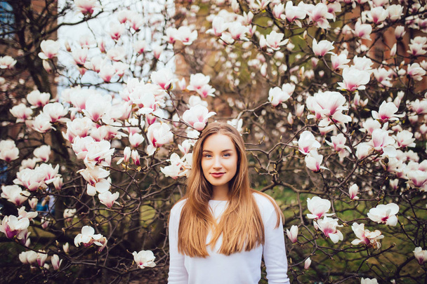Beauty woman standing on background Magnolia blossoming flowers. - Photo, Image