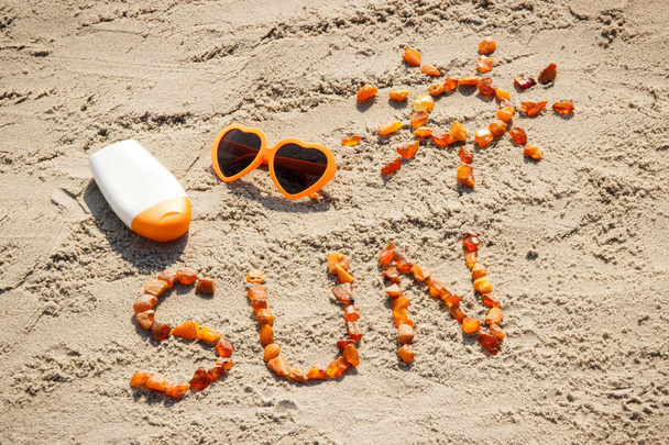 Word and shape of sun, sunglasses with sun lotion on sand at beach, summer time - Photo, image