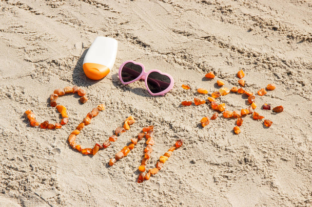 Word and shape of sun, sunglasses with sun lotion on sand at beach, summer time - Photo, Image