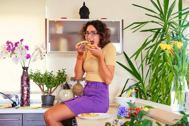 Brunette woman eating pizza in the kitchen - Photo, Image