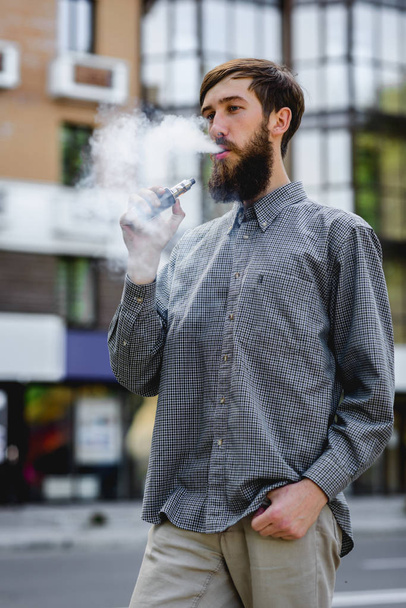 Men model with beard vaping an electronic cigarette. Vaping outdoors. Safe smoking. Young hipster vaper. - Фото, зображення
