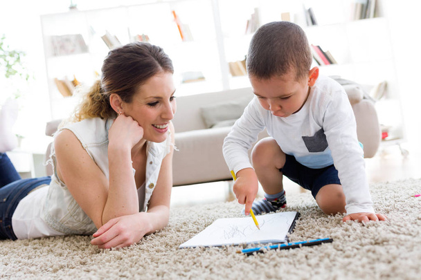 Beautiful young mother and her son drawing at home. - Фото, изображение
