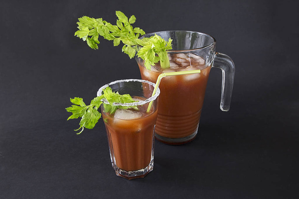 a glass with a cocktail "Bloody Merry" with ice and a sprig of celery on a black background - Photo, Image