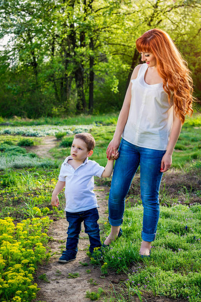 Young mother walks with her little son in the garden. Mother's Day concept - Photo, Image