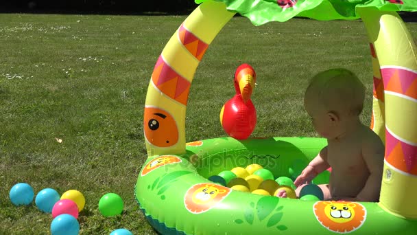 Nevetve csecsemő baba fröccsenő víz a medencében teljes színes labdák. 4k - Felvétel, videó