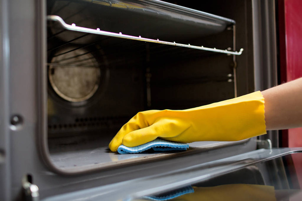 hand with rag cleaning oven at home kitchen - Foto, afbeelding