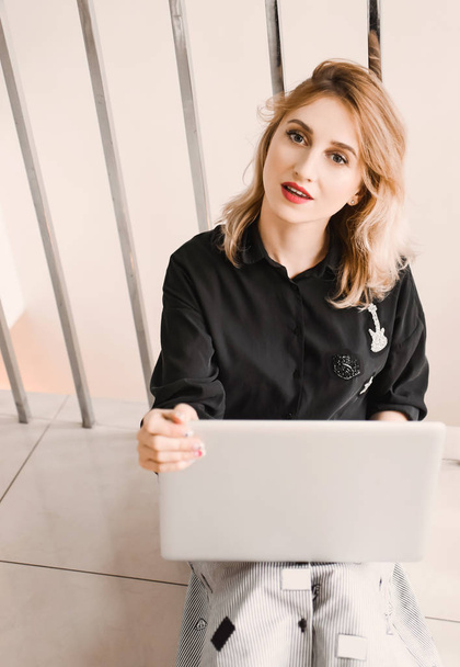Girl young beautiful blonde hipster with red lips  inside  in black blouse  holds smart laptop tablet using - Zdjęcie, obraz