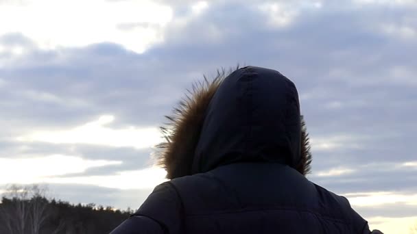 a csuklyás férfi áll, aki a kamera vissza a háttérben a természet során naplemente-lassú mozgás - Felvétel, videó