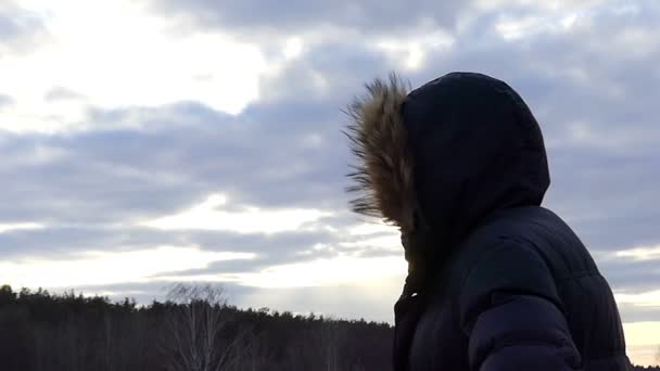 bir adam bir kukuleta ile yavaş çekimde bir gün batımı sırasında arka plan doğa üzerinde yan duruyor - Video, Çekim
