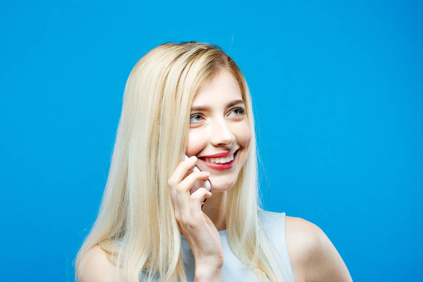 Portrait of Smiling Woman Talking by Mobile Phone on Blue Background. Blonde with Long Hair with Smartphone in Studio. - Fotografie, Obrázek