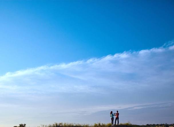 Genç sevgili çift gökyüzü arka plan üzerinde gözlük ile bir tepede duruyor - Fotoğraf, Görsel