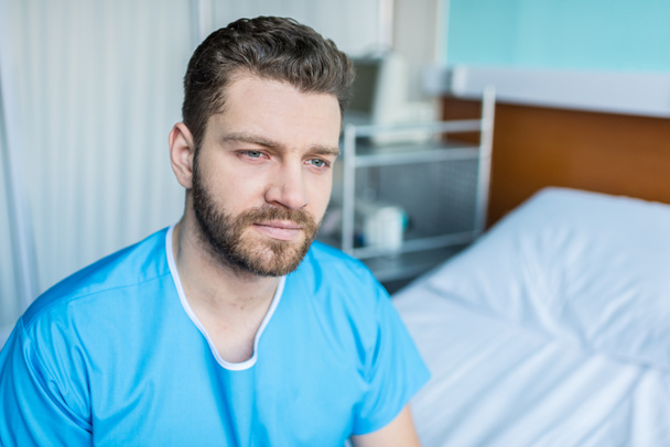 άρρωστος άνθρωπος κάθεται στο κρεβάτι του νοσοκομείου - Φωτογραφία, εικόνα