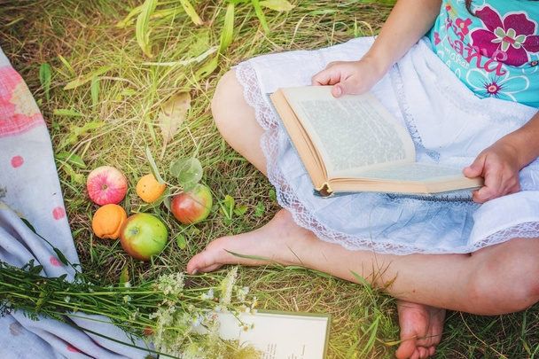 Κορίτσι με ένα βιβλίο συνεδρίαση για το γρασίδι στον κήπο το καλοκαίρι. - Φωτογραφία, εικόνα