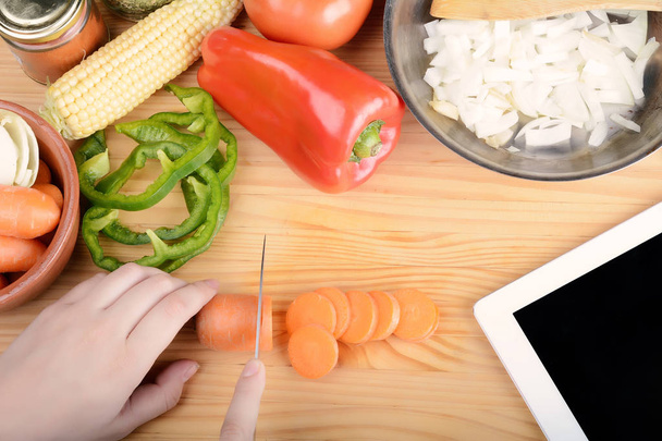 Person cutting a carrot with vegetables and digital tablet. - Photo, Image
