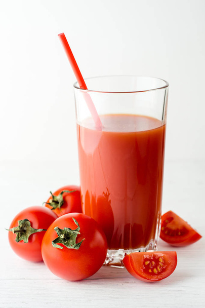 Tomato juice in glass and fresh tomatoes on white wooden table. - Foto, afbeelding