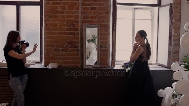 Девушка снимает красивых моделей в черном свадебном платье у красной кирпичной стены у окна. Фотосессия за кулисами
. - Кадры, видео