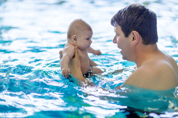 Happy middle-aged father swimming with cute adorable baby in swimming pool. - Foto, Imagen