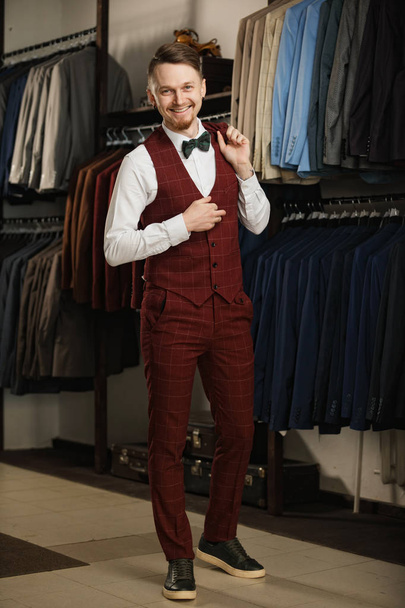 Handsome young bearded businessman in classic suit. A young stylish man in a jacket. It is in the showroom, trying on clothes, posing. Advertising photo - Photo, image